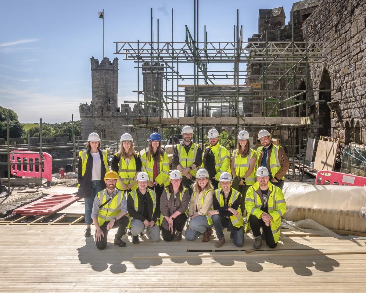 a group of people in hard hats and hi vis pose in front of a castle