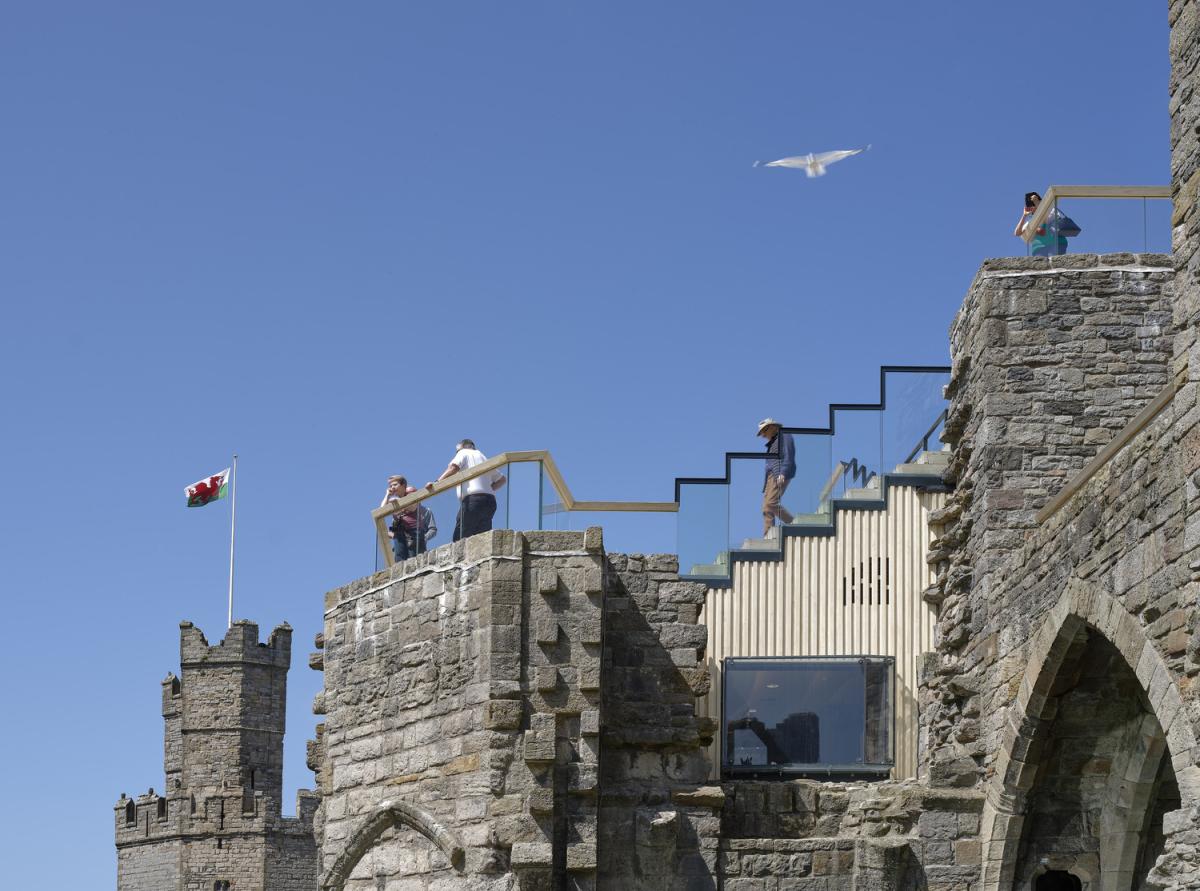 External view of the King's Gate area of Caernarfon Castle showing people walking down the new wooden stairs and being able to view through the glass balconies. 