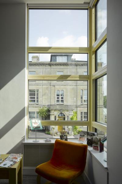a glazed corner of a classroom looks out over a historic building. An orange chair sits in the corner.