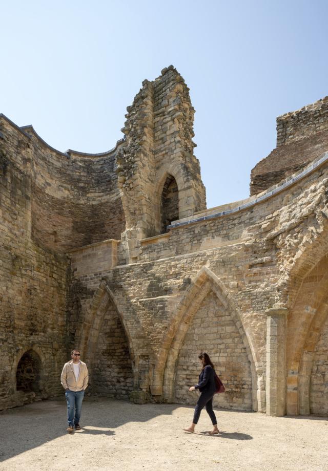 a man and lady walk in front of a historic stone wall with an arch
